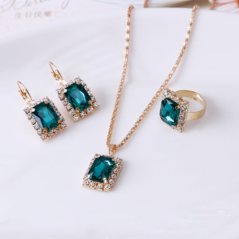 Elegant three-piece jewelry set with turquoise pendant necklace, earrings, and ring on a plate.