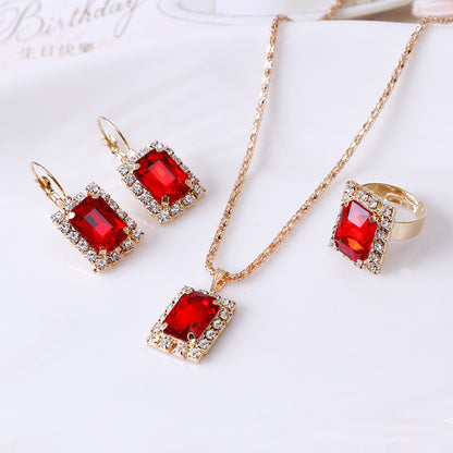 Elegant three-piece jewelry set featuring red crystal necklace, earrings, and ring in golden alloy.