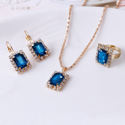 Elegant three-piece jewelry set with sapphire blue pendant necklace, earrings, and ring on a plate.