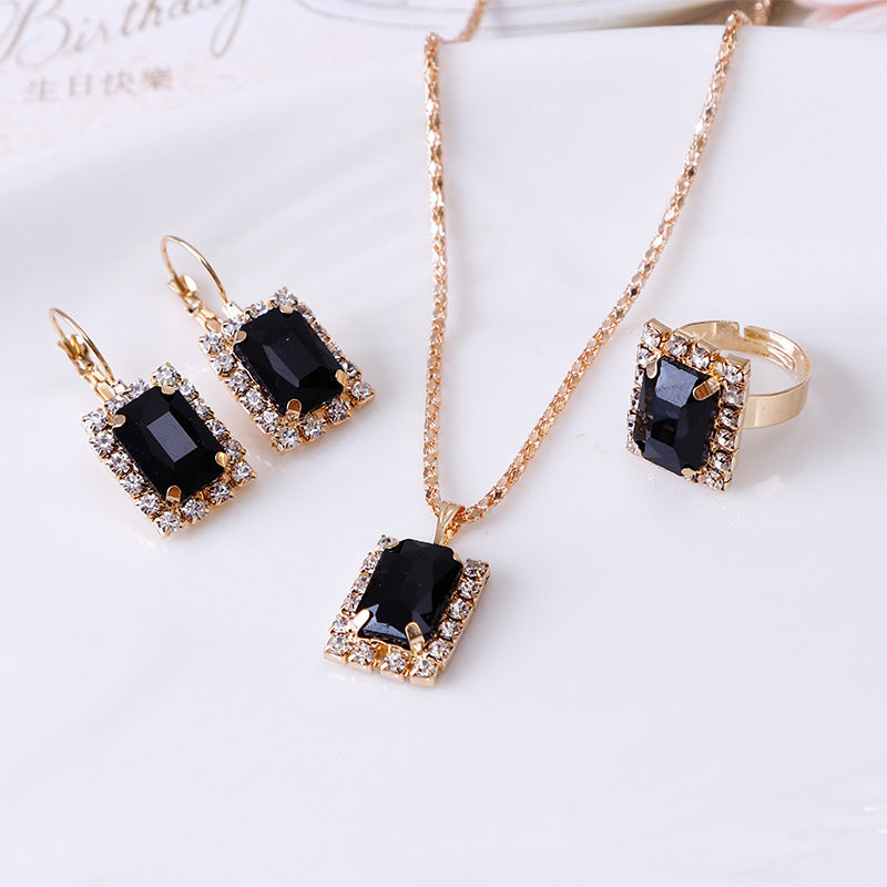 Elegant three-piece jewelry set featuring black crystal necklace, earrings, and ring on a delicate curb chain.