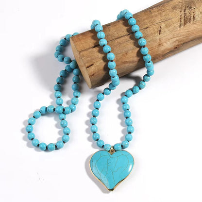 Vintage handmade knotted beaded necklace with turquoise heart pendant on wooden display.